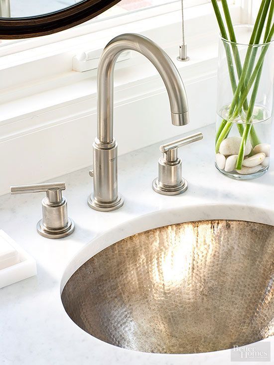 a white stone countertop plus a hammered brass undermount sink of an oval shape for a glam and chic look