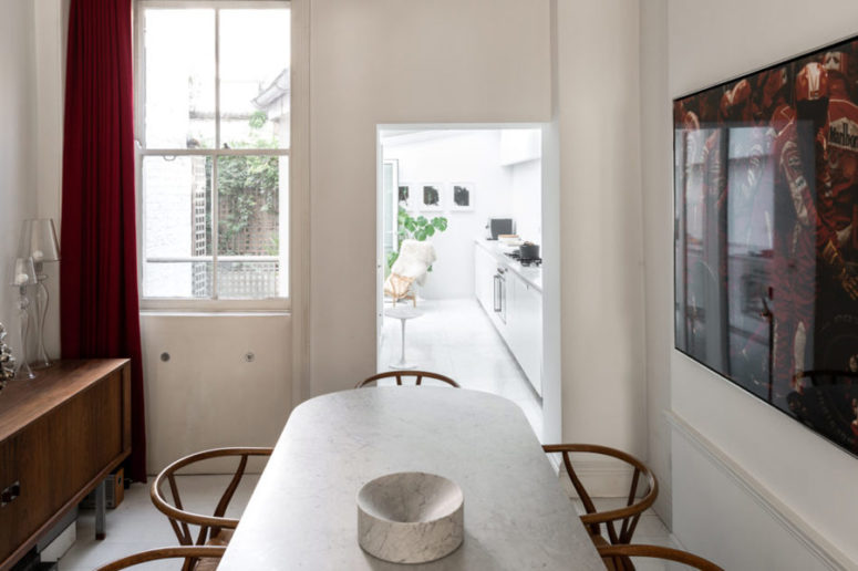 The dining room is done with a rich stained sideboard, a neutral table, wooden chairs, red curtains and a bold artwork