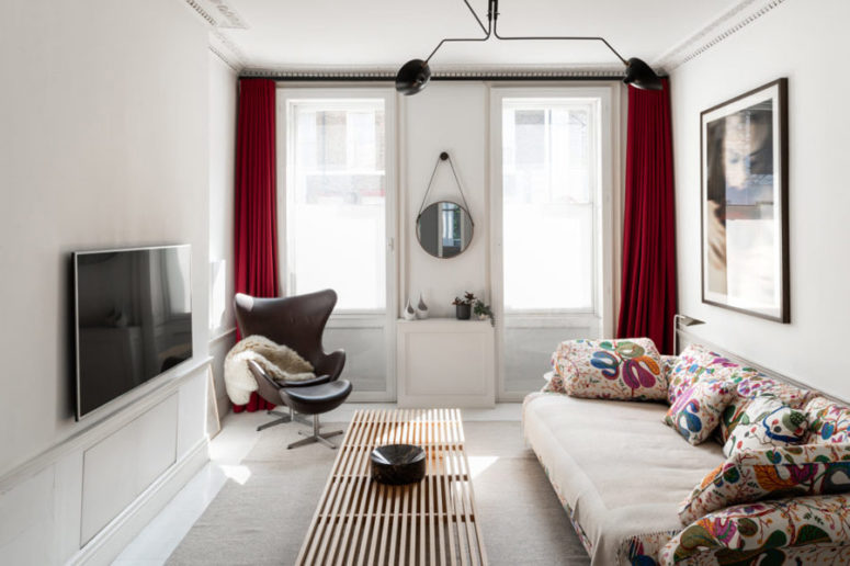 The TV room is done with red curtains, a brown leather chair and footstool and a fun and whimsy floral sofa