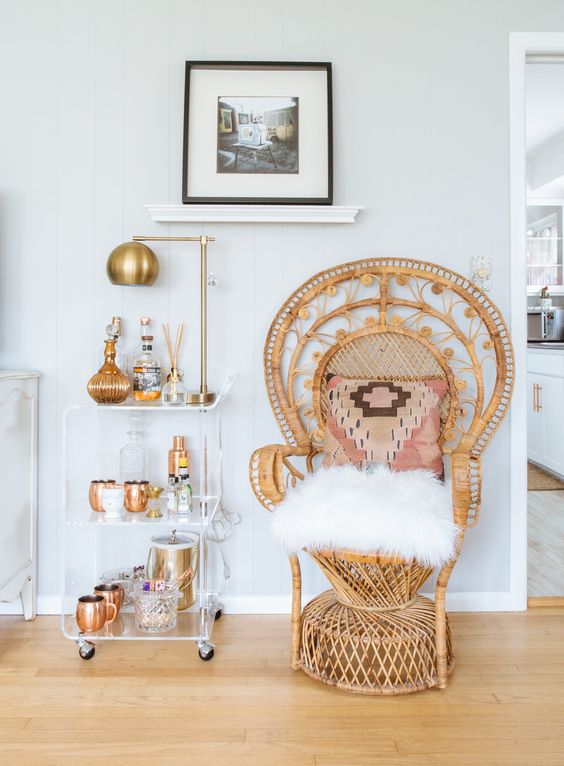 a chic drink space with a peacock chair with a bright pillow and faux fur plus a clear acryl bar cart