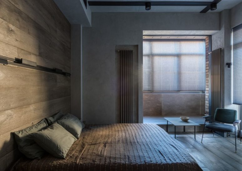 This bedroom features a comfy sleeping space, a wooden wall and some light-filled bathing space incorporated