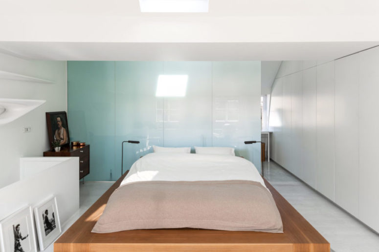 This bedroom is done with a blue glass wall, a platform bed, a rich stained dresser, black and white artworks