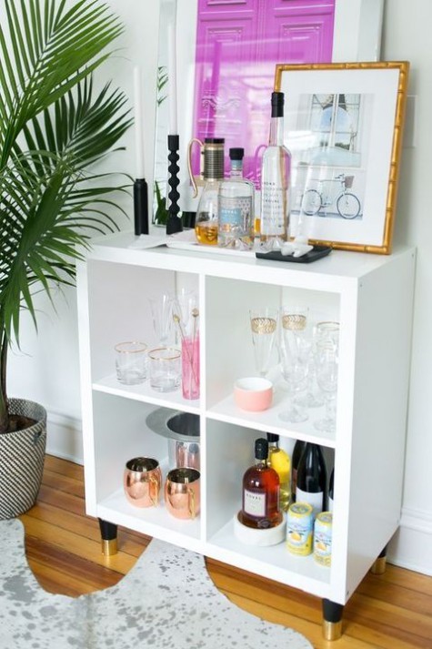a stylish home bar made of an IKEA Kallax shelf with elegant gilded legs features much storage