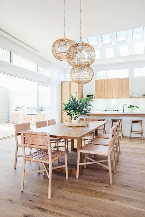 woven leather chairs, light-colored wood and roudn wicker lampshades over the dining space make it feel beachy