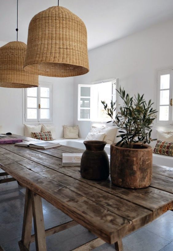 a relaxed coastal space done in white, with a weathered wood table and wicker lamps over it for a relaxed feel