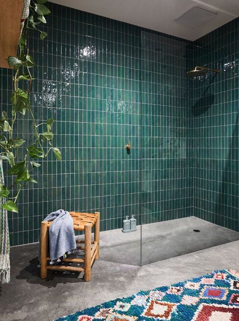 a bold boho bathroom with an emerald stacked tile shower space, a concrete floor, a bright rug, a woven stool and a potted plant