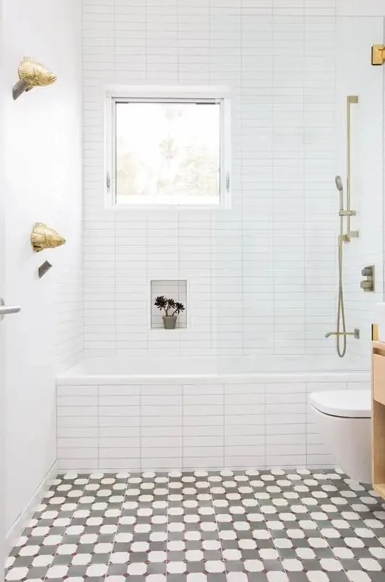 a bright bathroom with a mosaic floor, white tiles with built-in shelves, a window and gold hardware