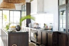 a chic tropical kitchen with dark stained cabinets, baskets, wicker lampshades, tropical plants and a striped rug