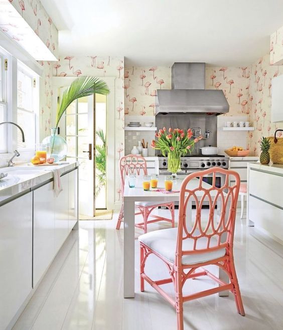 a creative tropical kitchen with flamingo wallpaper, sleek white cabinets, pink rattan chairs, tropical plants