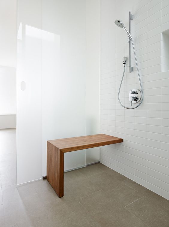 a creative wooden bench addded to a pure white shower with frosted glass doors