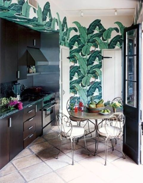 a dark kitchen with bright tropical leaf wallpaper, forged furniture and black countertops for a bold look