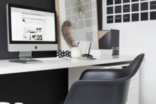 a laconic Nordic home office with a black statement wall and chair, a black noteboard, a white desk and a relaxed artwork