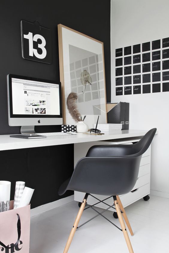 a laconic Nordic home office with a black statement wall and chair, a black noteboard, a white desk and a relaxed artwork