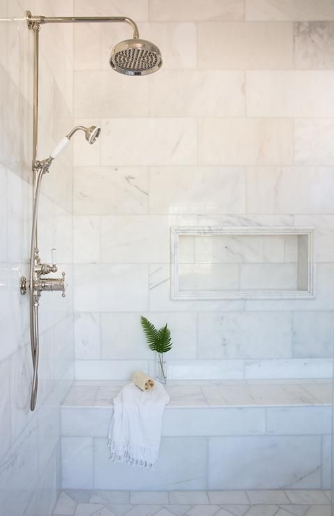 a marble tiled shower bench is positioned beneath a marble tiled niche lined with marble pencil tiles