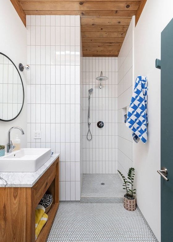 a mid-century modern bathroom with stacked skinny tiles and penny ones, a stained vanity, a round mirror and a potted plat