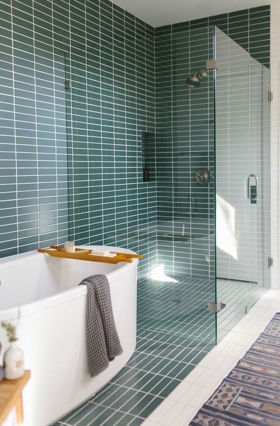 a mid-century modern bathroom with teal skinny tiles, a white tub and a printed rug is a very welcoming space