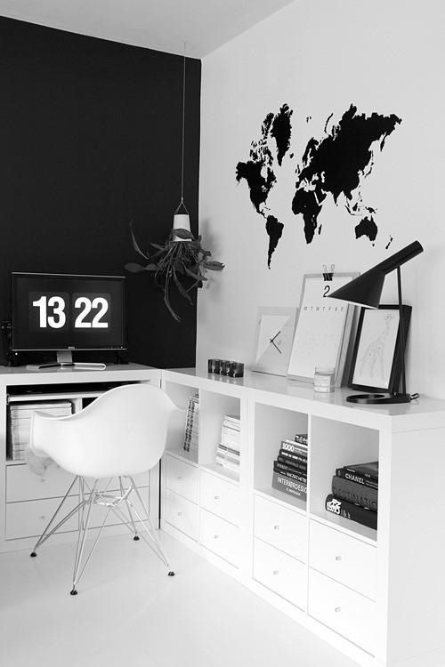 a minimalist black and white home office with a black statement wall, a map on the wall, a comfortable storage unit and a white chair