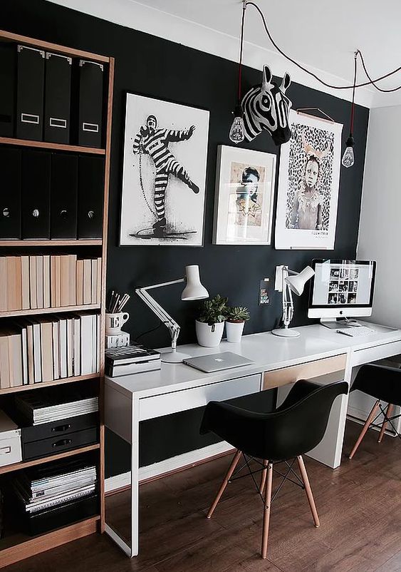 a moody contemporary home office with a black statement wall, a white desk, artworks and a shelving unit