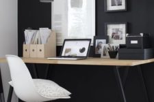 a moody home office with a black statement wall, pendant lamps, a desk with black legs and black framed artworks