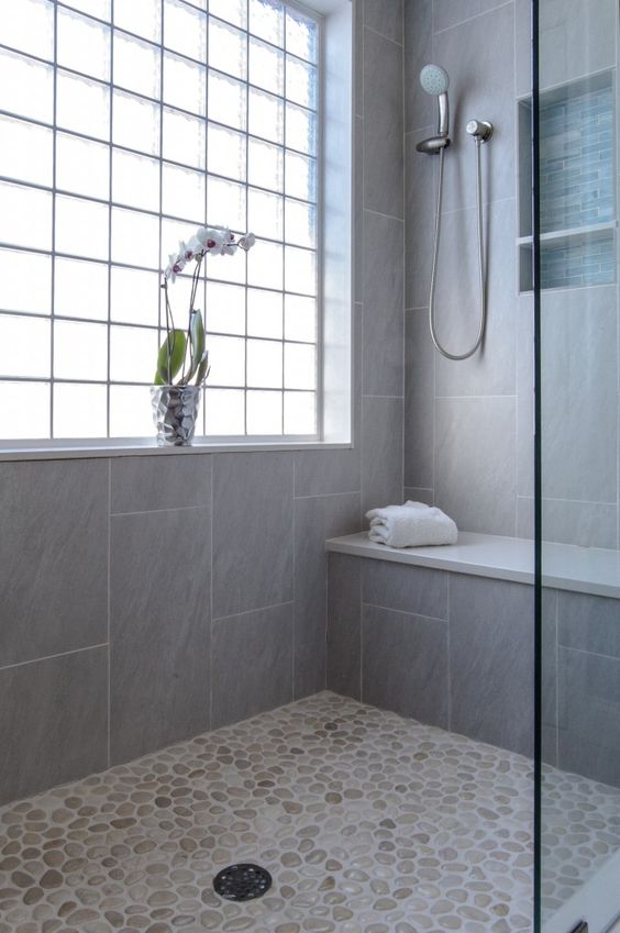 a neutral shower space with a pebble floor and grey tiles, a window with framing and a built in bench a neutral shower space with a pebble floor and grey tiles, a window with framing and a built-in bench