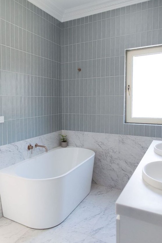a serene contemporary bathroom with grey stacked tiles, an oval tub, a white vanity and a sink is a lovely and airy space