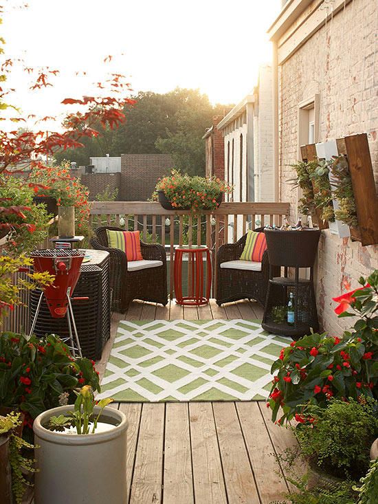 a small and bright deck with simpel woven furniture, colorful upholstery, a grill and potted greenery and flowers