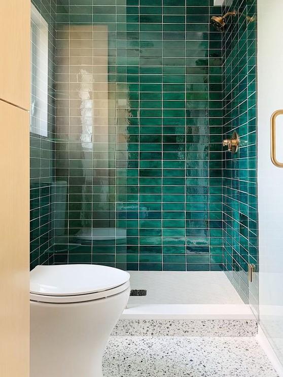 a small bathroom with an emerald stacked tile shower, a white terrazzo floor and brass touches for a super chic look