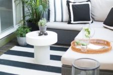 a small black and white deck with an L-shaped upholstered bench, a coffee table, a candle lantern and potted greenery