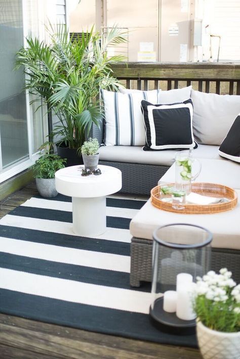 a small black and white deck with an L-shaped upholstered bench, a coffee table, a candle lantern and potted greenery