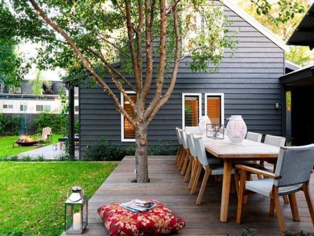 a small deck turned into a dining space, with modern furniture, a living tree, a candle lantern and pillows