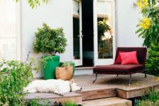 a small deck with a comfortable burgundy lounger, a couple of bright planters and a relaxed pup