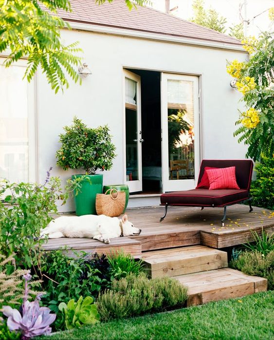 a small deck with a comfortable burgundy lounger, a couple of bright planters and a relaxed pup