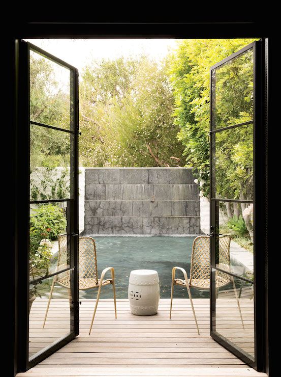 a small deck with a couple of rattan chairs and a stylish coffee table in boho style in front of the pool