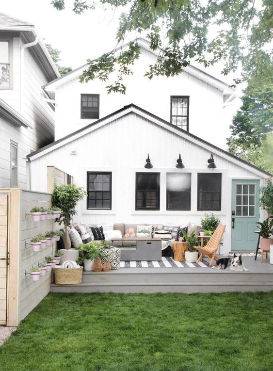 a small deck with a sectional sofa, potted greenery, a chest, a rug and some folding chairs