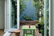 a small deck with green furniture, potted greenery and a rattan side table feels very welcoming and secluded
