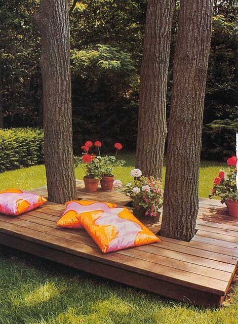 a small deck with living trees, potted greenery and blooms and colorful pillows is a gorgeous relaxing retreat