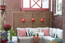 a small fall-inspired deck with an L-shaped upholstered bench, colorful pillows and potted blooms