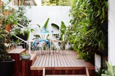 a small rich stained wooden deck with simple metal and plywood furniture and lots of greenery around for freshness
