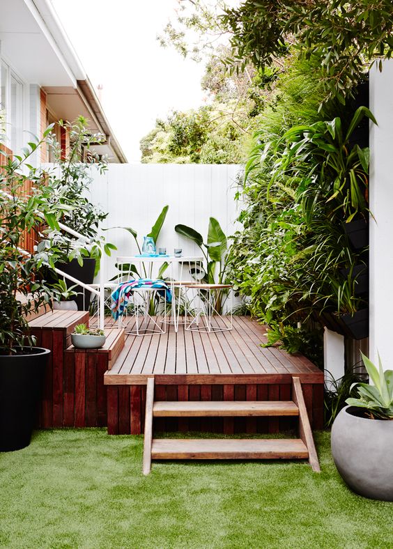 a small rich stained wooden deck with simple metal and plywood furniture and lots of greenery around for freshness