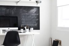 a stylish eclectic home office with a chalkboard, a white desk, a black chair and some white boxes for storage