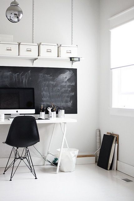a stylish eclectic home office with a chalkboard, a white desk, a black chair and some white boxes for storage