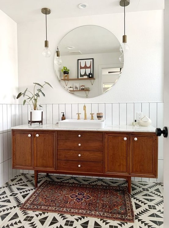 a stylish mid-century modern bathroom with white skinny tiles, geo tiles on the floor, a boho rug, a wooden vanity and pendant lamps