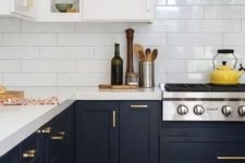 a trendy two tone kitchen with white and black cabinets, white countertops and gold hardware plus a white subway tile backsplash