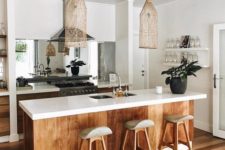 a tropical kitchen with white cabinets, stained wood covering the kitchen island, wooden stools, wicker lamps and a mirror backsplash