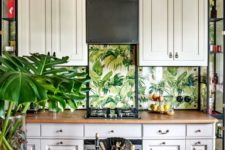 a vintage tropical kitchen with creamy cabinets, a wooden table, black rattan chairs and tropical leaf wallpaper