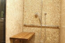 a warm-toned shower with the same tiles everywhere and a folding wooden bench on the wall