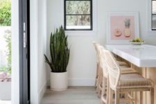 a white tropical kitchen with rattan stools, wicker pendant lamps plus a tropical plant in a pot
