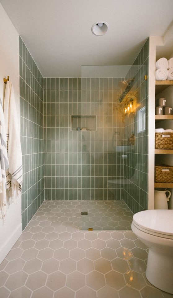an earthy bathroom with skinny green and grey hexagon tiles, a large shower space, built-in shelves and white appliances