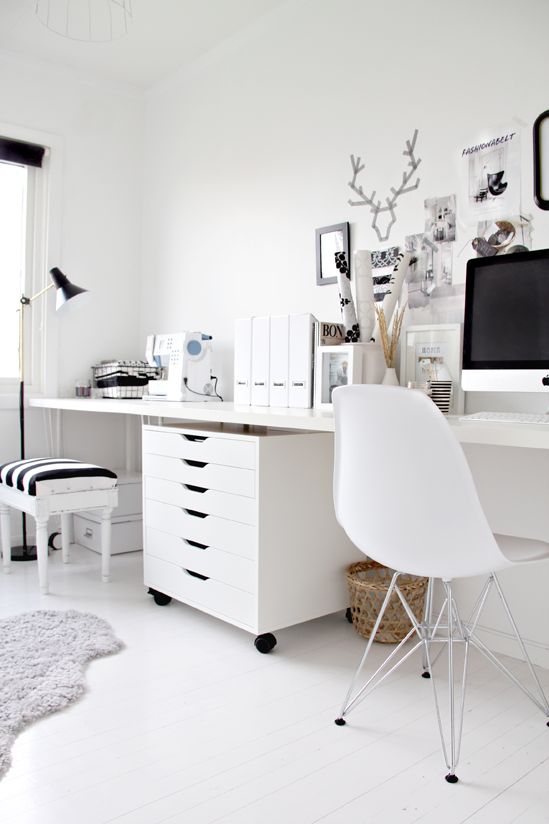 an eclectic black and white home office with white furniture, a black lamp, frames for artworks and a stool with a striped seat