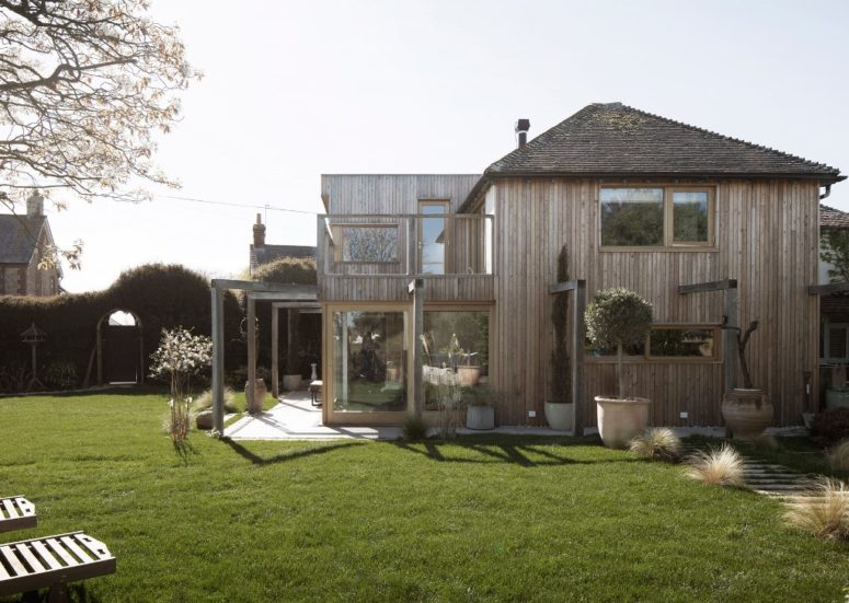 The outdoor space features a manicured lawn with potted greenery and blooms, loungers and a living fence